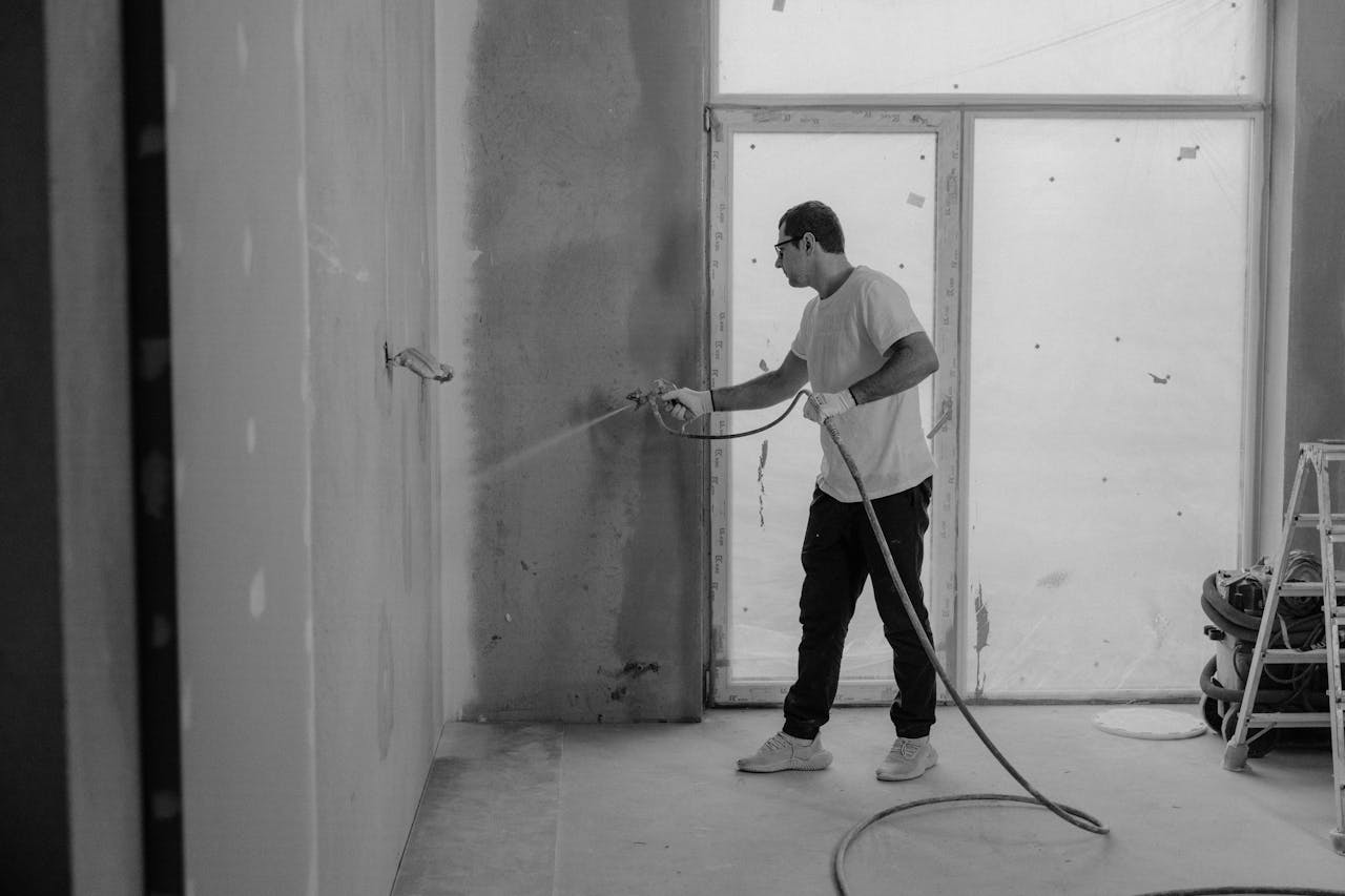 A worker paints an interior wall with a spray gun during a renovation project.